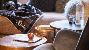 A cozy room with a view of a mountain landscape through a window, a plush sofa, a small round table with a glass of water, and a book. - das Alois (Tux)