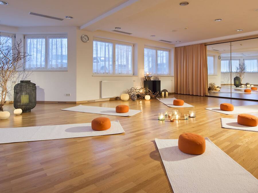 Un estudio de yoga con suelos de madera, esterillas, cojines naranjas, velas y un espejo grande.