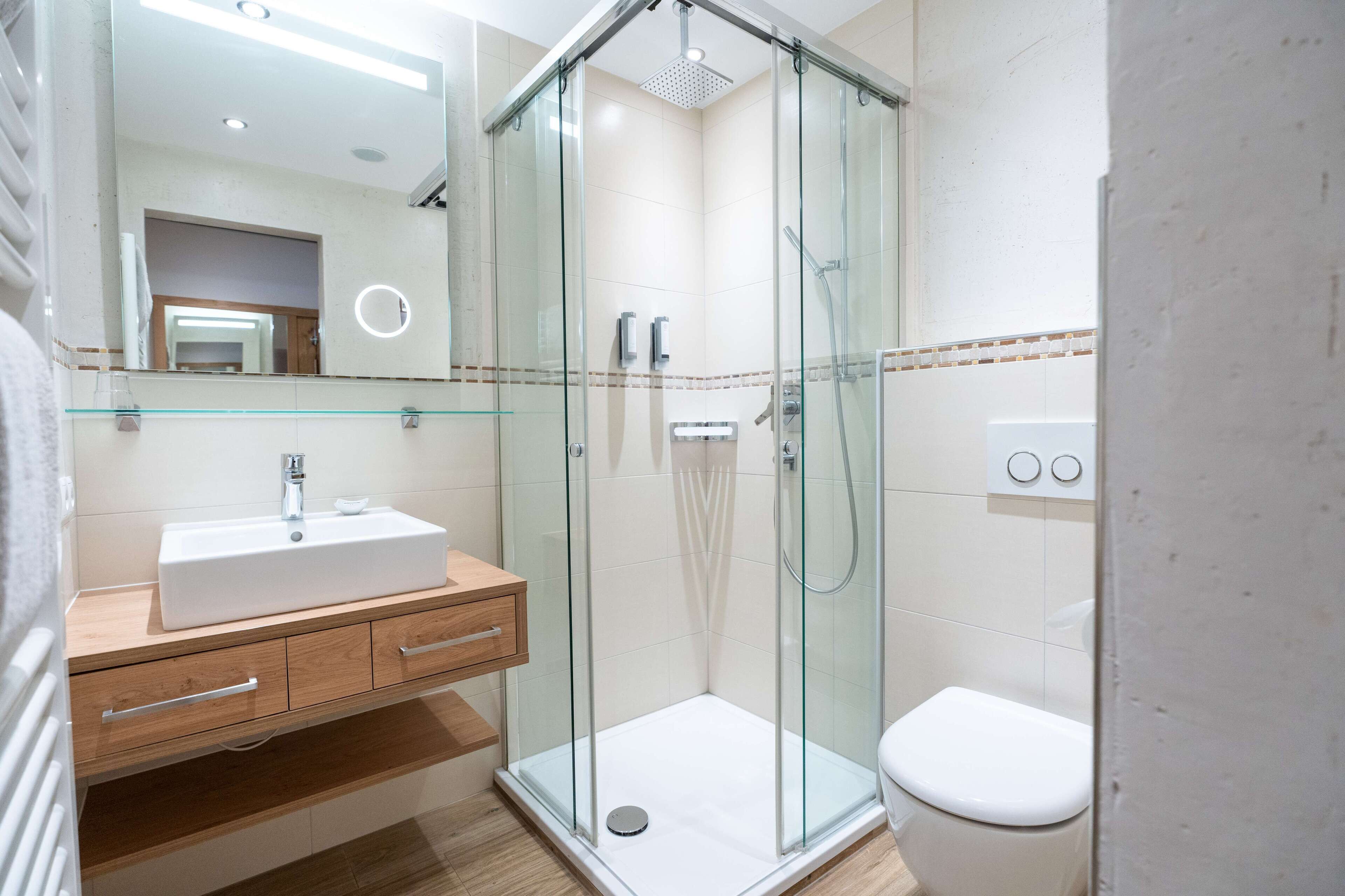 Un baño moderno con ducha envuelta en vidrio, un lavamanos blanco y un inodoro.