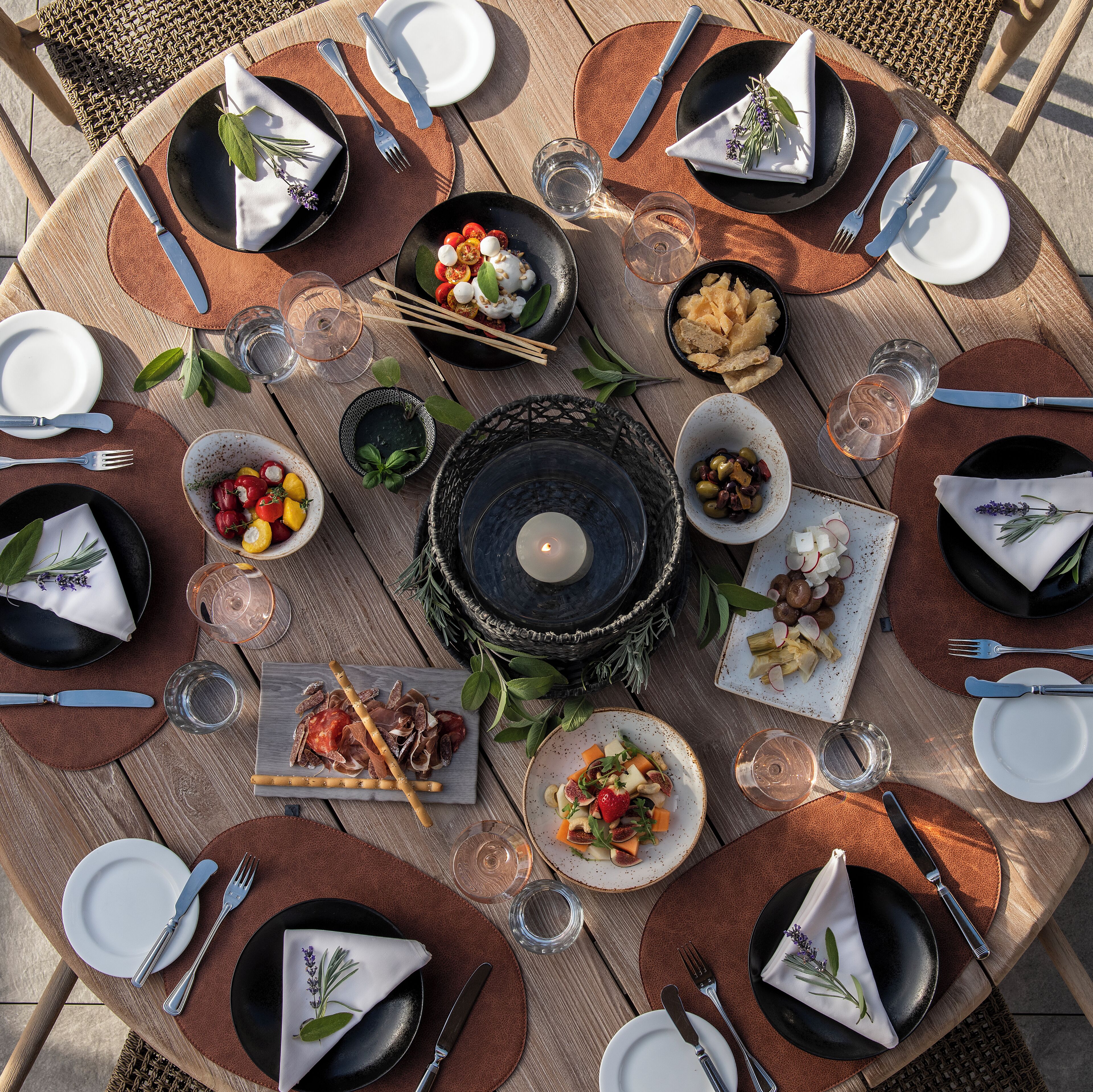 A round wooden table set for a meal with plates, cutlery, and various dishes.