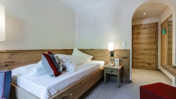 Una habitación de hotel con una cama de madera, una mesita de noche con una lámpara, un teléfono y un banco rojo.