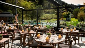 An outdoor dining area with tables set for guests, surrounded by a glass enclosure with a view of a mountainous landscape. - das Alois (Tux)