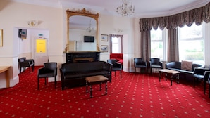A room with a red carpet, black sofa, and multiple chairs. - The Maemar Hotel (Bournemouth)