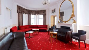 A room with a red carpet, a black leather sofa, a red sectional sofa, a black armchair, and a round wooden table. - The Maemar Hotel (Bournemouth)