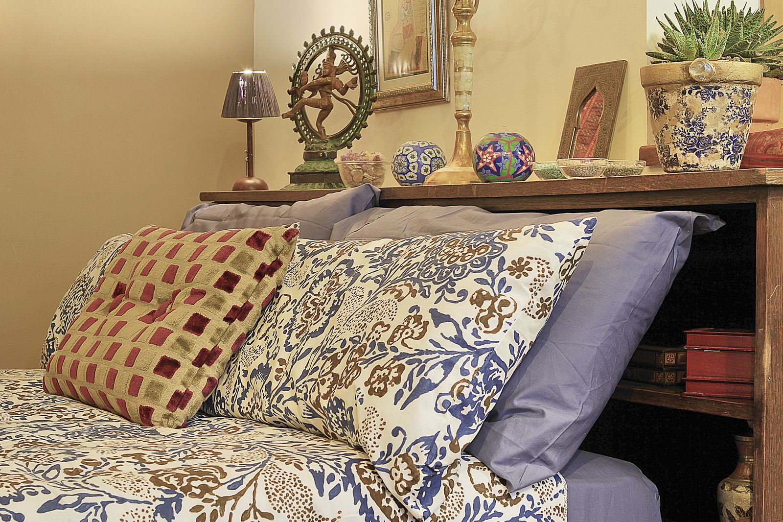 Un sofá con cojines estampados, un espejo decorativo y una mesita con lámpara y adornos.