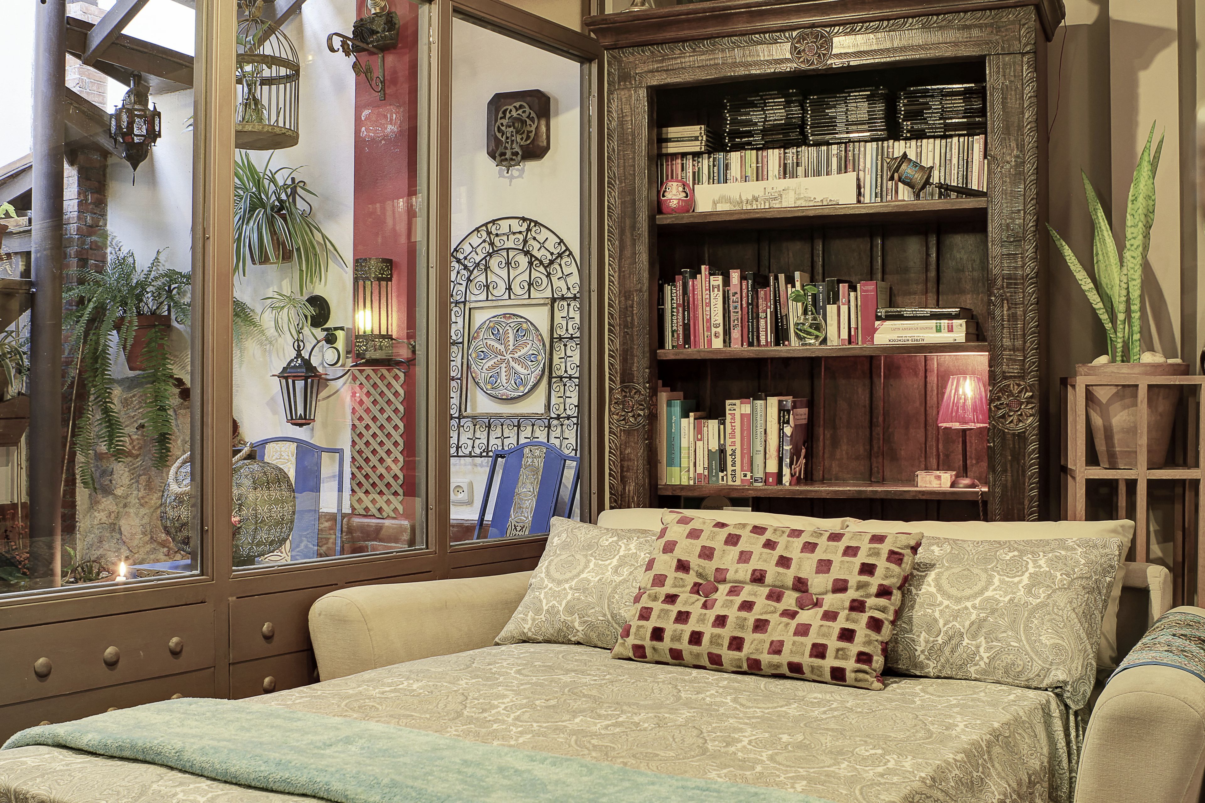 A cozy room with a large window, a bookshelf, and a bed with patterned bedding.