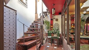 Una escalera con barandilla metálica, techo rojo y vista a un cuarto con mesa y sillas.