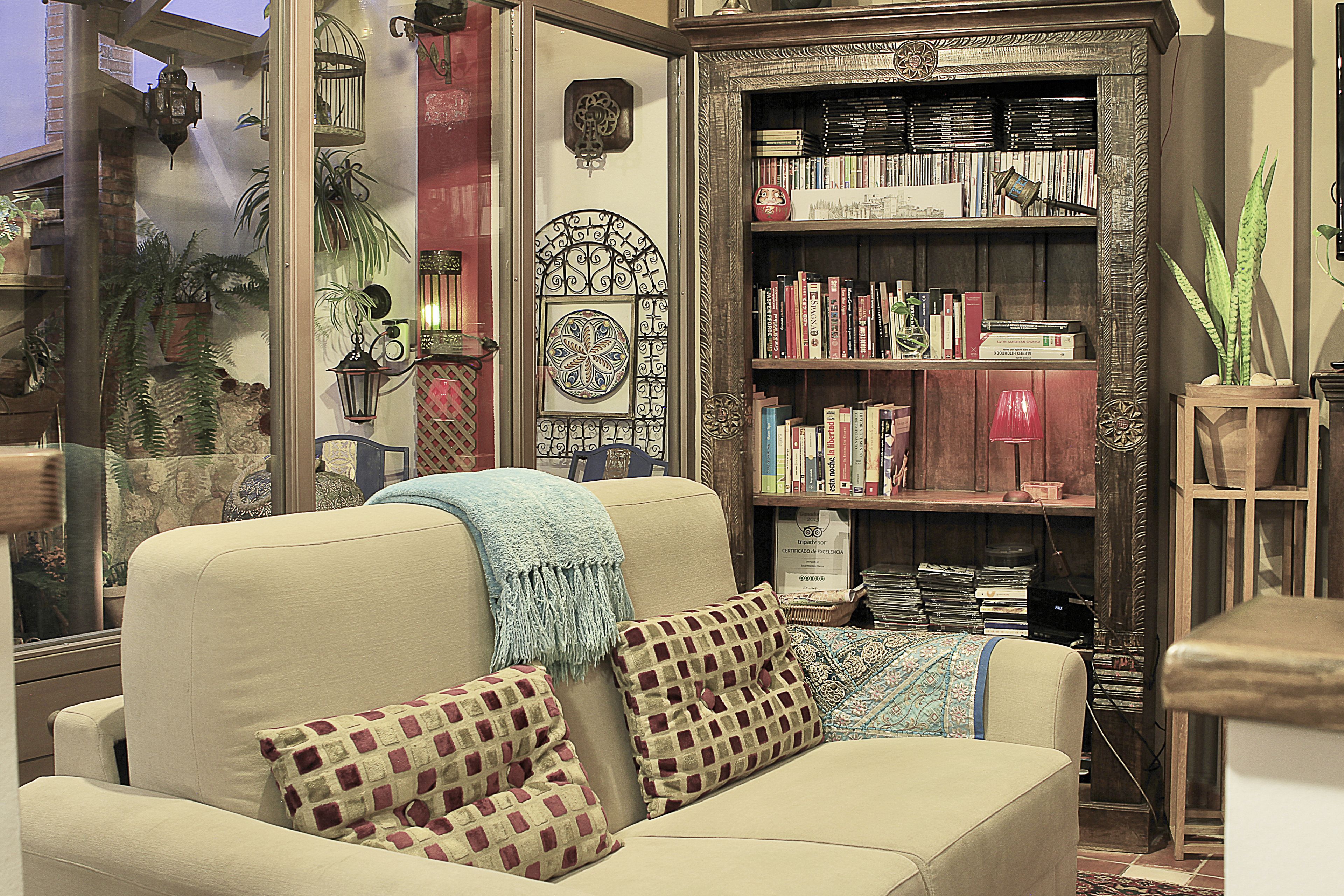 Ein gemütliches Wohnzimmer mit einem beigefarbenen Sofa, gemusterten Kissen, einem Bücherregal voller Bücher und dekorativer Wandkunst.