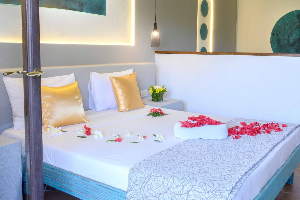 A bedroom with a large bed, a bedside table with a vase of flowers, and a painting on the wall.