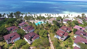 Vista aérea de un complejo turístico con varias casas, una piscina y una playa.