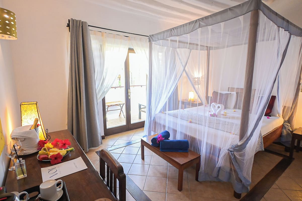 A hotel room with a bed under a canopy, a dining table with a menu, and a view of the outside.