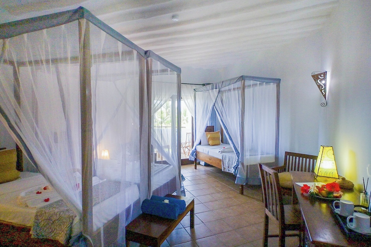 A room with two beds, each with a canopy, a small table with a lamp, and a chair.