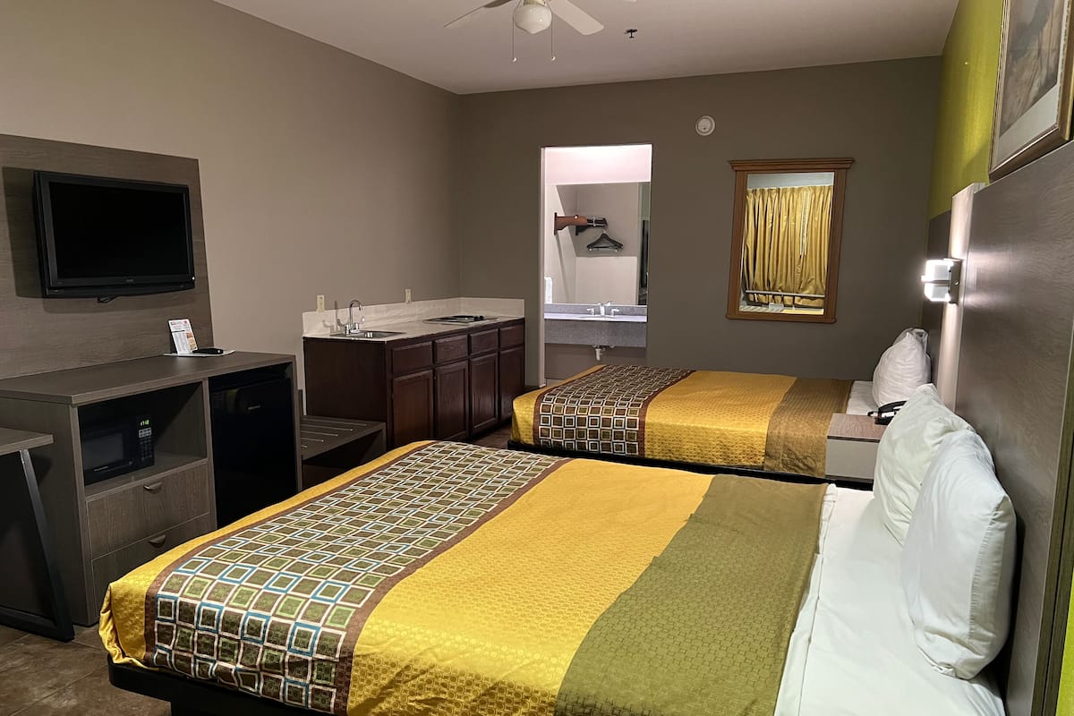 A hotel room with two beds, a desk, a television, a mirror, and a kitchenette.