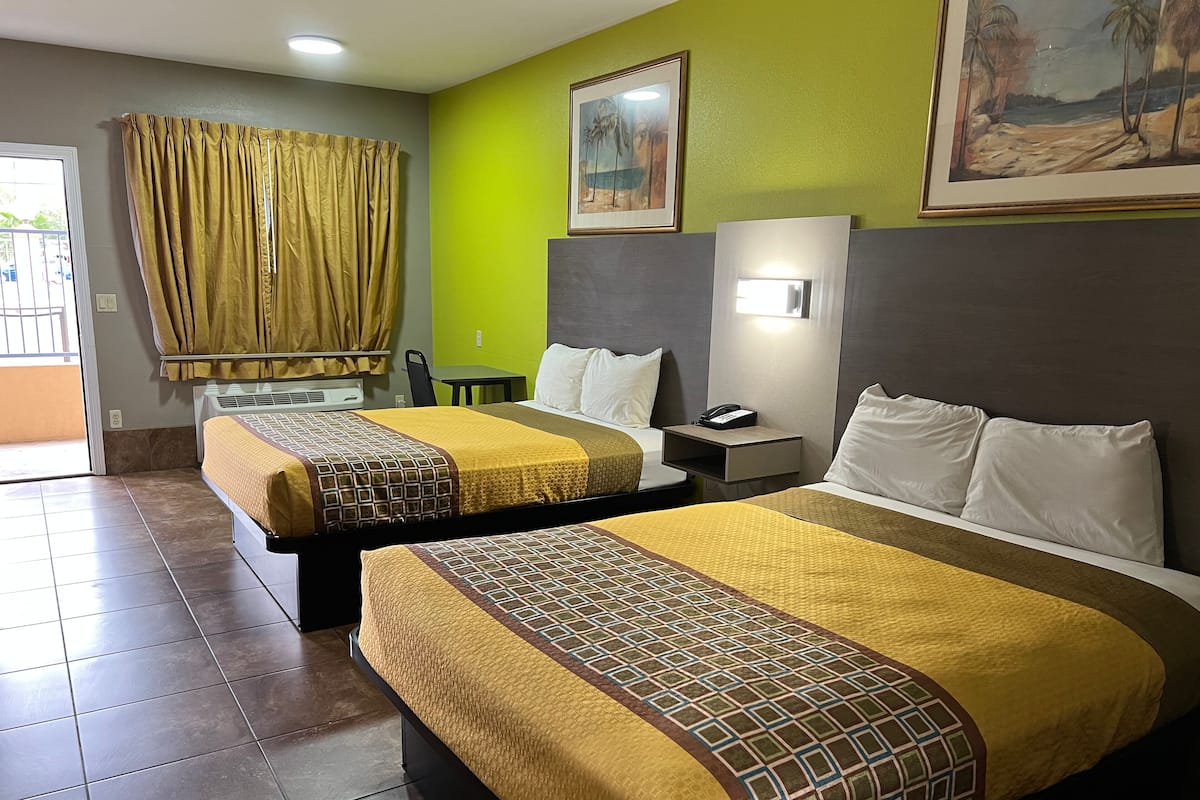 A hotel room with two beds, a desk, a chair, and a painting on the wall.