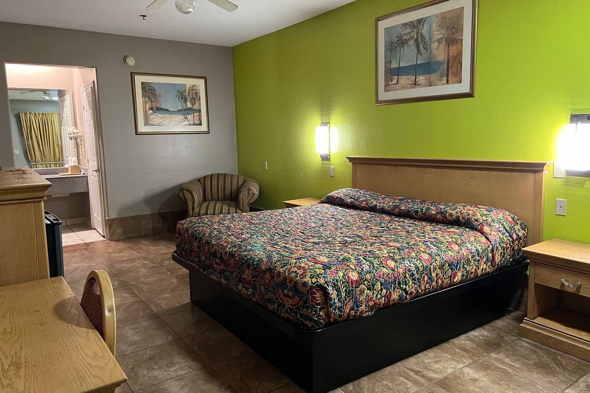 A hotel room with a bed, a chair, a desk, and a ceiling fan.