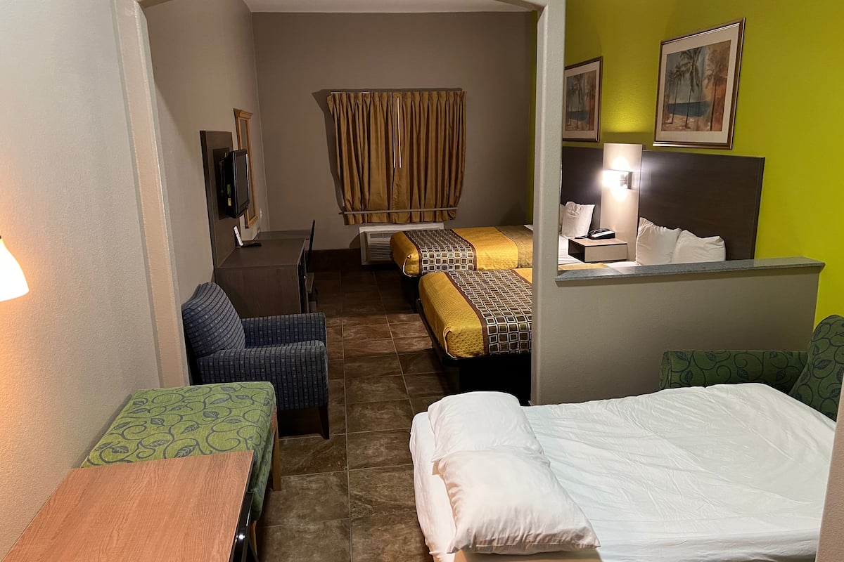 A hotel room with a bed, a desk, a chair, a TV, and a bathroom with a shower curtain.