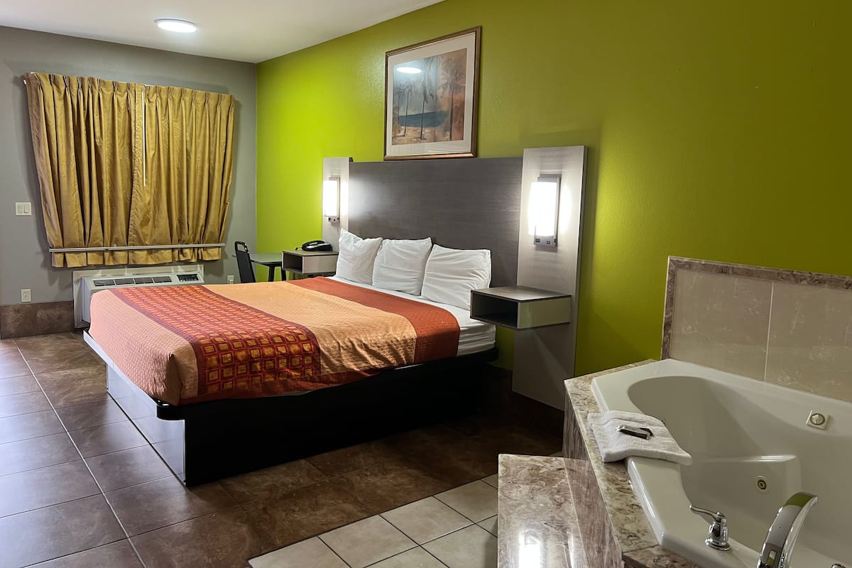 A hotel room with a bed, bedside table, nightstand, and a bathroom with a bathtub and sink.