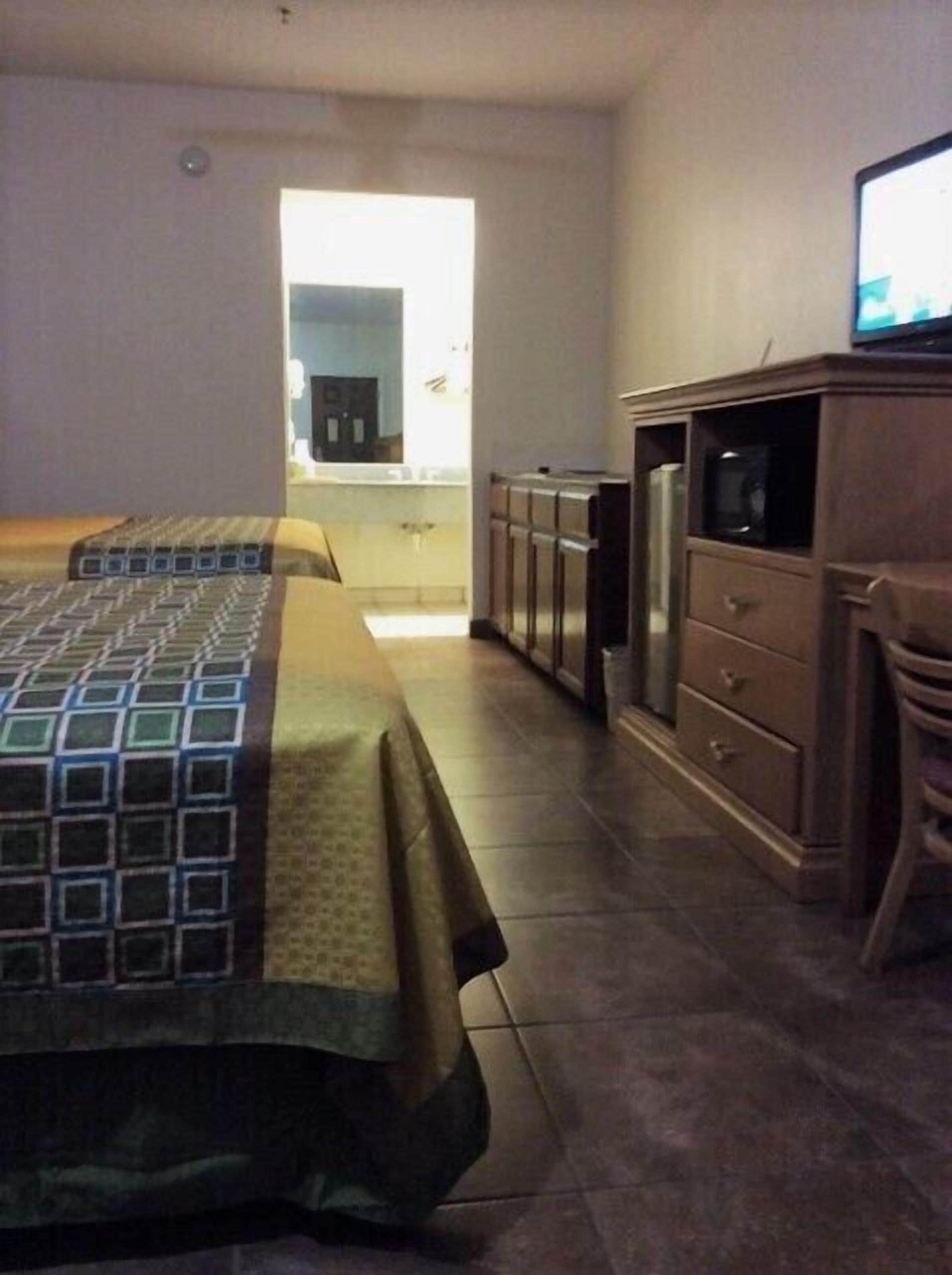 A hotel room with a bed, a dresser, a television, and a kitchenette area.