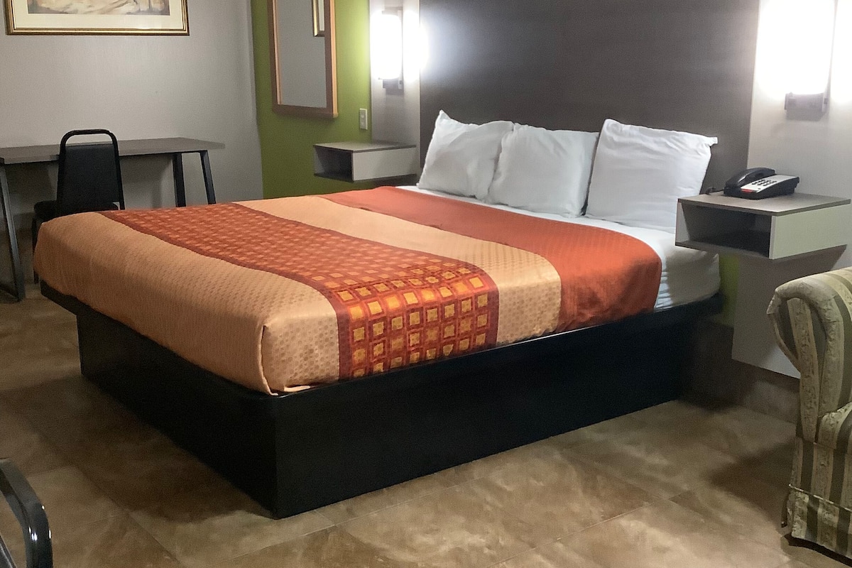 A hotel room with a bed, a desk, a chair, and a nightstand with a phone.