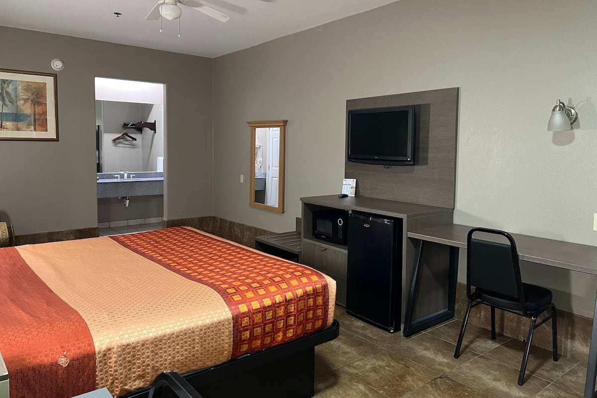 A hotel room with a bed, desk, chair, television, and a ceiling fan.