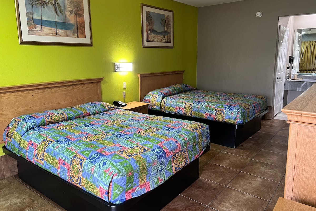 A hotel room with two beds, a small desk, a nightstand, and a bathroom visible through an open door.