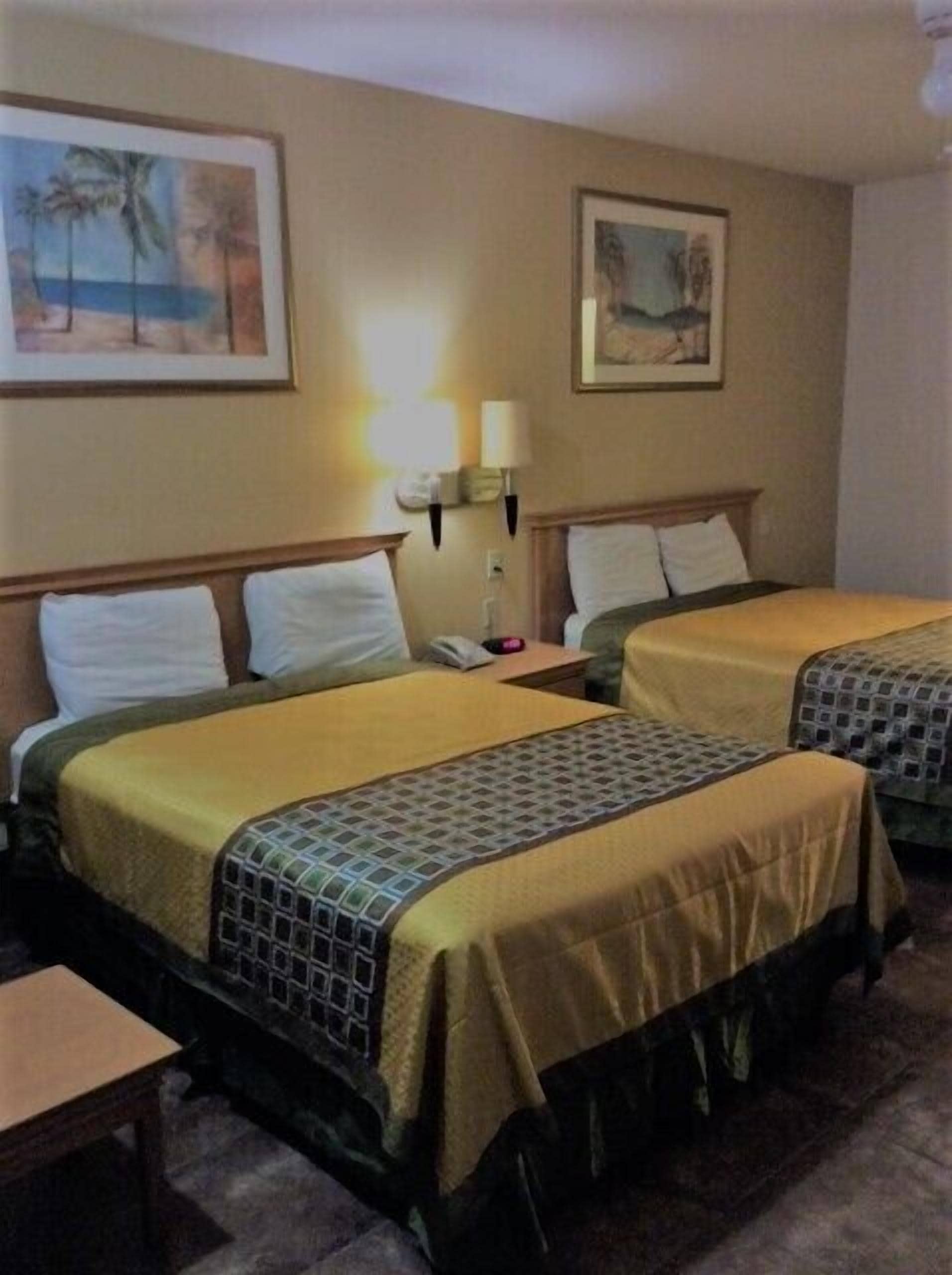 A hotel room with two beds, a nightstand, a lamp, and two framed pictures on the wall.