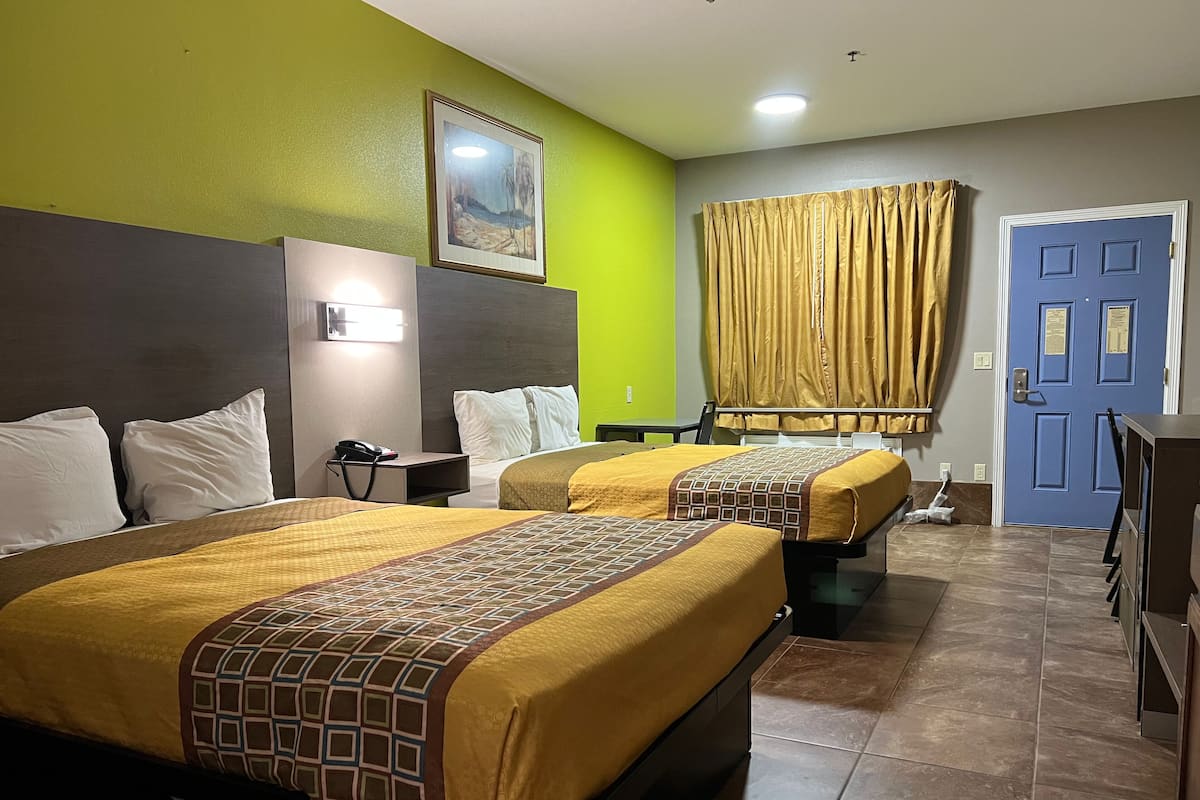 A hotel room with two beds, a nightstand with a phone, a painting on the wall, a blue door, and a curtain.