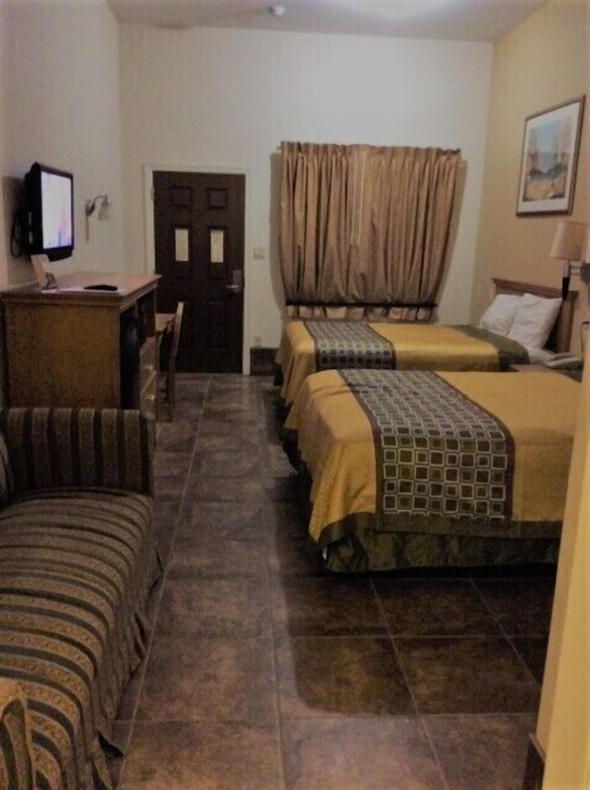 Ein Hotelzimmer mit zwei Betten, einem Schreibtisch, einem Stuhl und einem Fernseher.