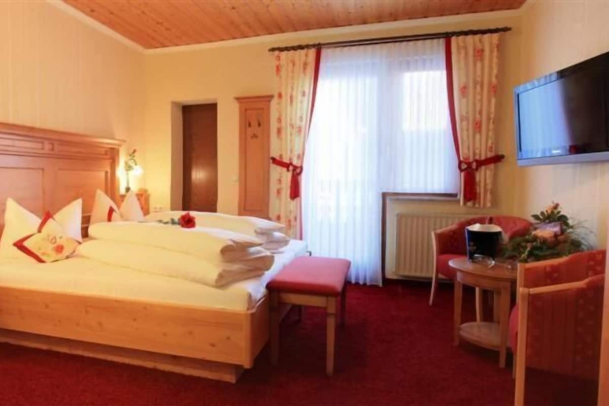 A hotel room with a wooden bed, a desk, a chair, a TV, and a radiator.