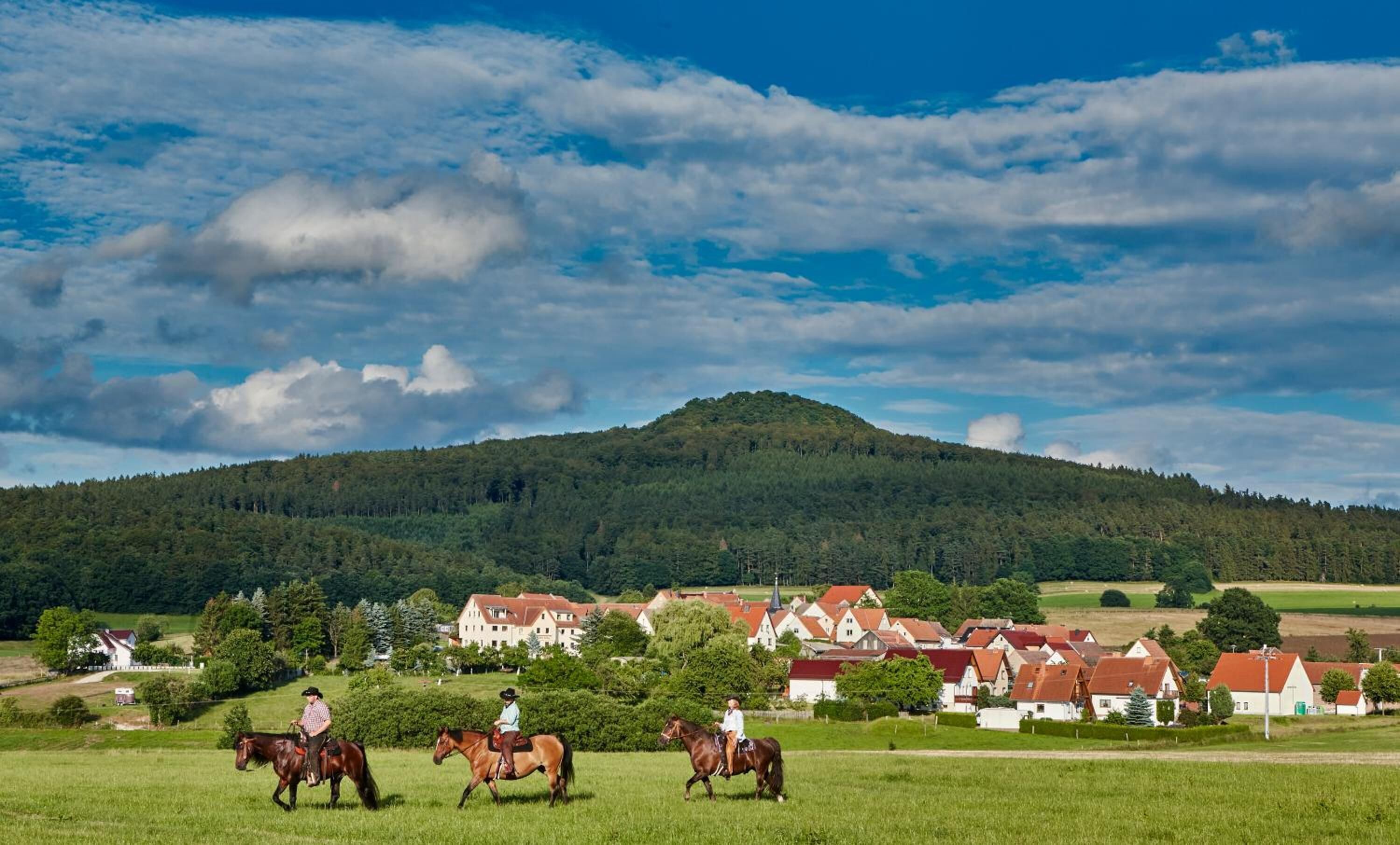 Landskab med en landsby, en bakke og tre personer til hest.
