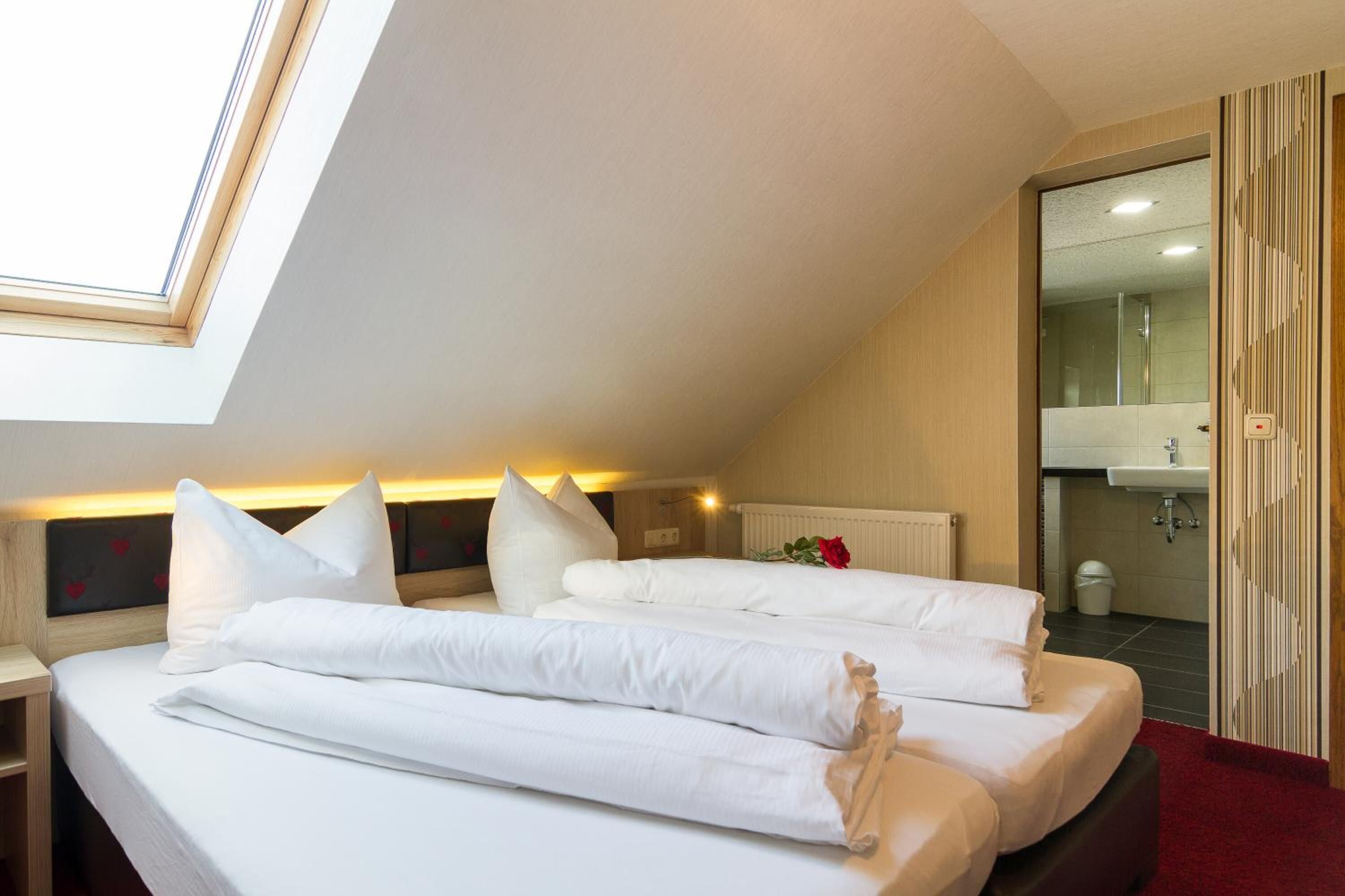 A hotel room with two beds, a skylight, a bathroom with a mirror and sink, and a red carpet.