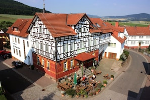 A traditional half-timbered building with a red-tiled roof, a courtyard with outdoor seating, and a view of the surrounding landscape. - Landhotel Zur Grünen Kutte (Dermbach)