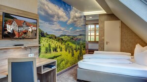 Habitación de hotel con cama, escritorio con computadora, televisor montado en la pared y un mural panorámico grande.