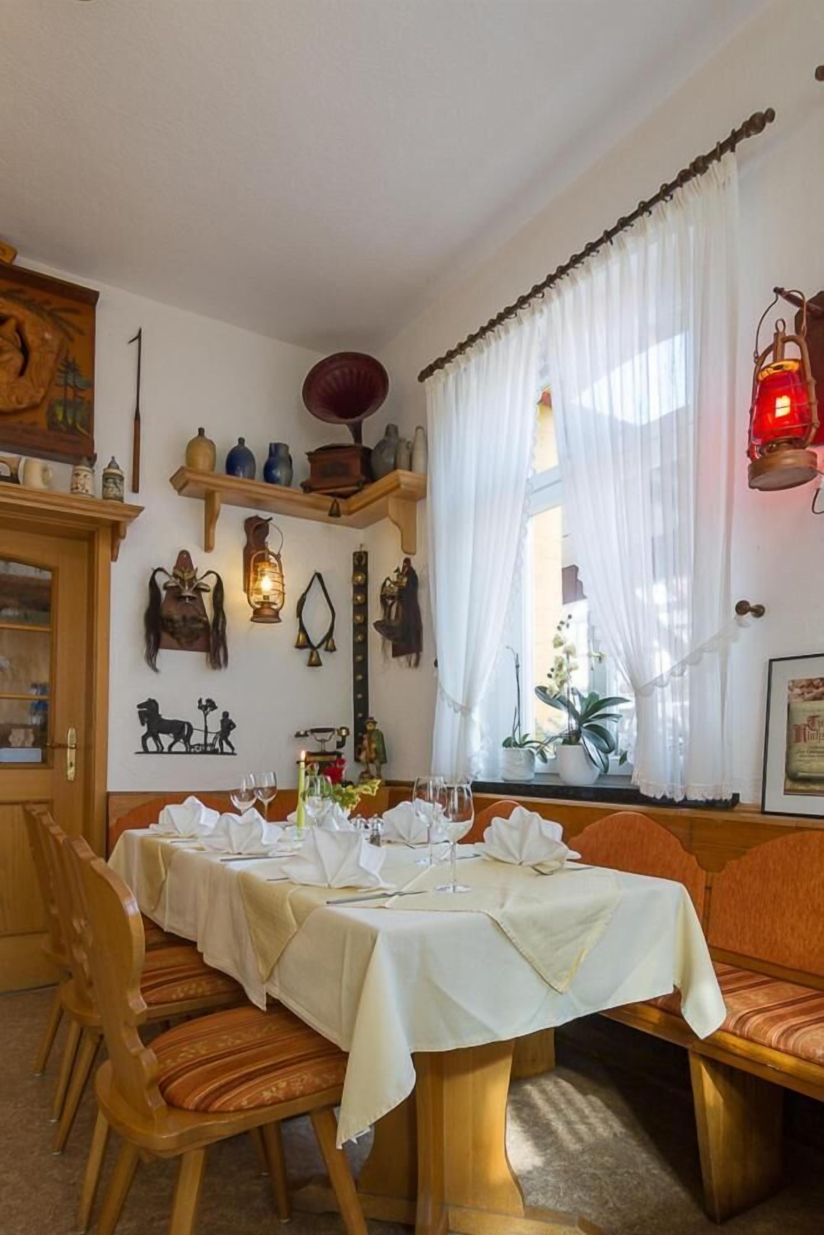 Ein Essbereich mit Tisch für zwei Personen, Holzsesseln, einem Fenster mit transparenten Vorhängen und Wanddekoration.