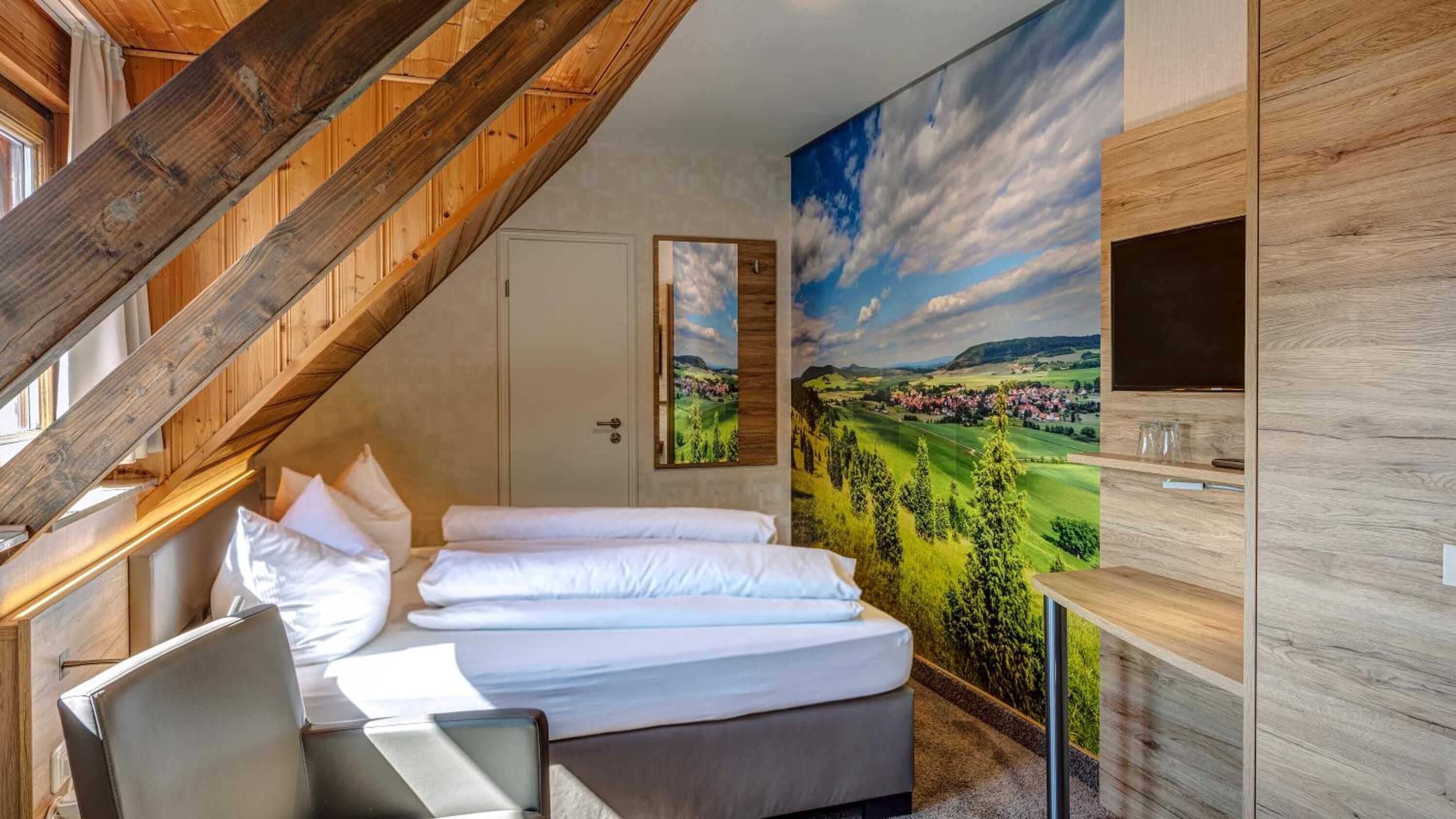 A bedroom with a bed, a desk, and a large landscape painting on the wall.