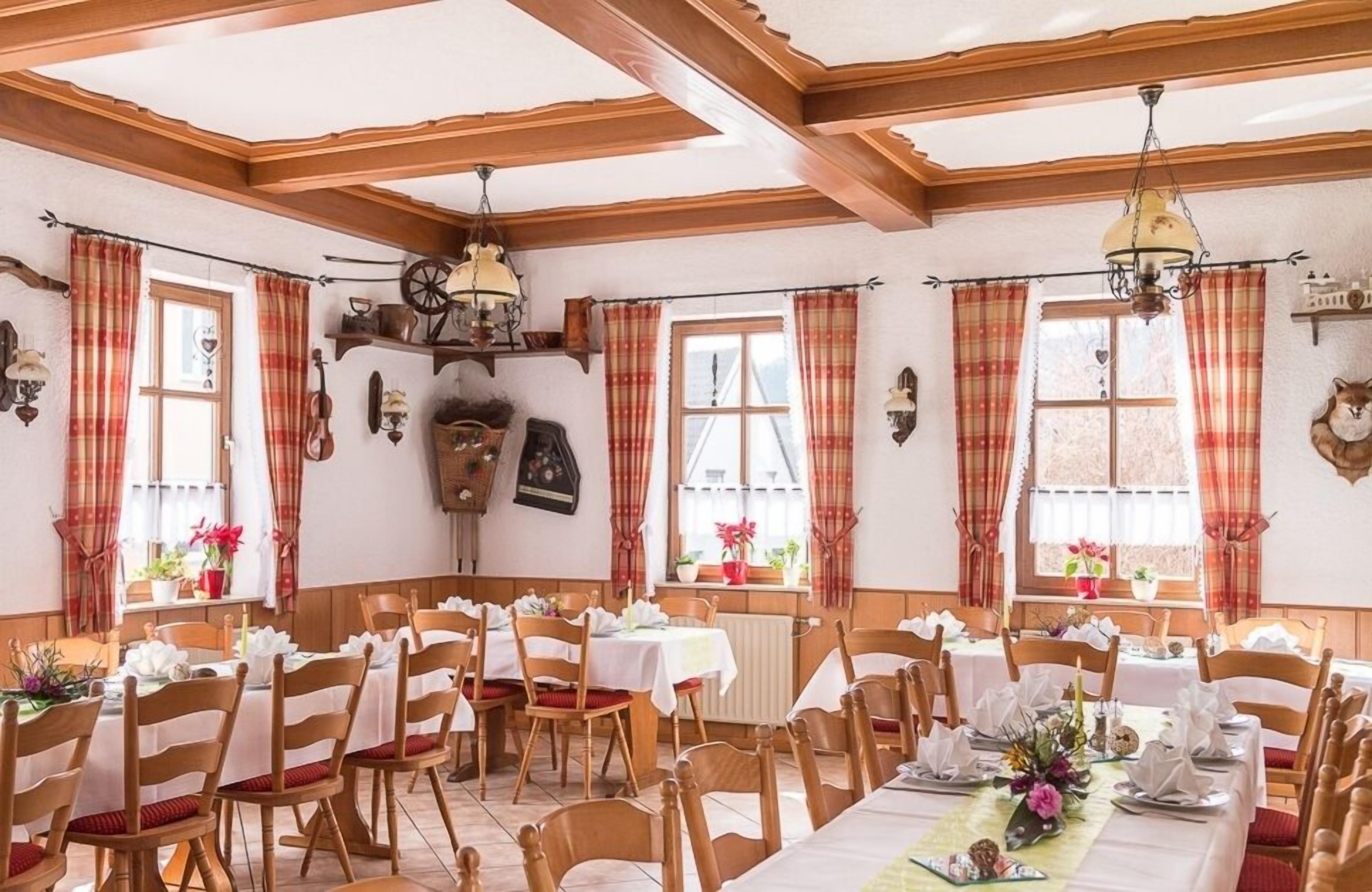 A dining area with wooden beams, plaid curtains, and tables set for a meal.