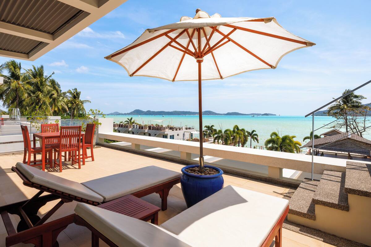 A balcony with a view of the ocean, a lounge area with chairs and a table, and a large umbrella.