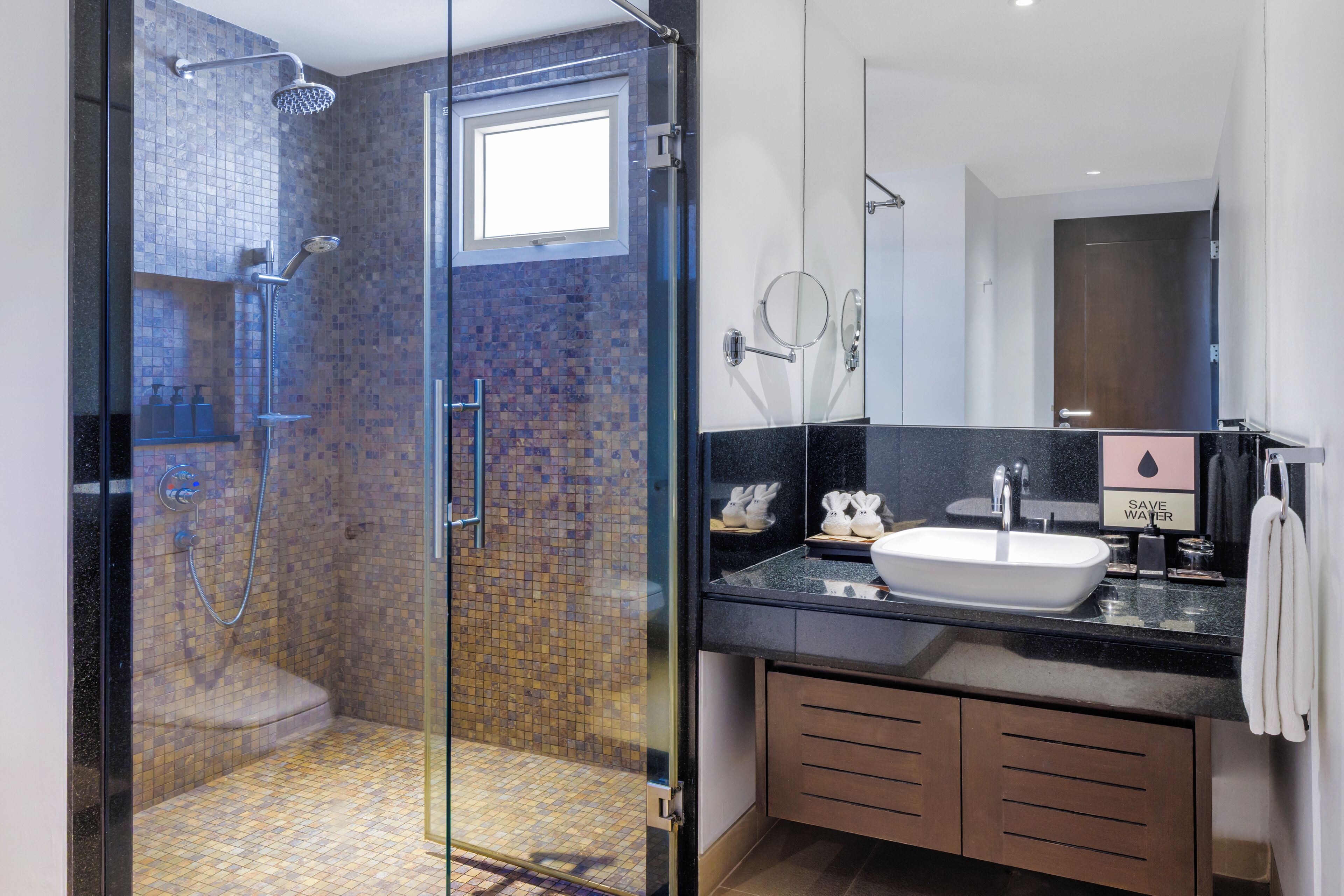 A modern bathroom with a glass-enclosed shower, a sink with a 'SAVE WATER' sign, and a large mirror.