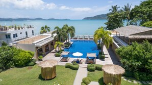 Un resort con una piscina grande, sillas de descanso y vistas al mar.