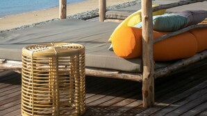 Una terraza de madera con un toldo, un taburete de mimbre y un cojín naranja.