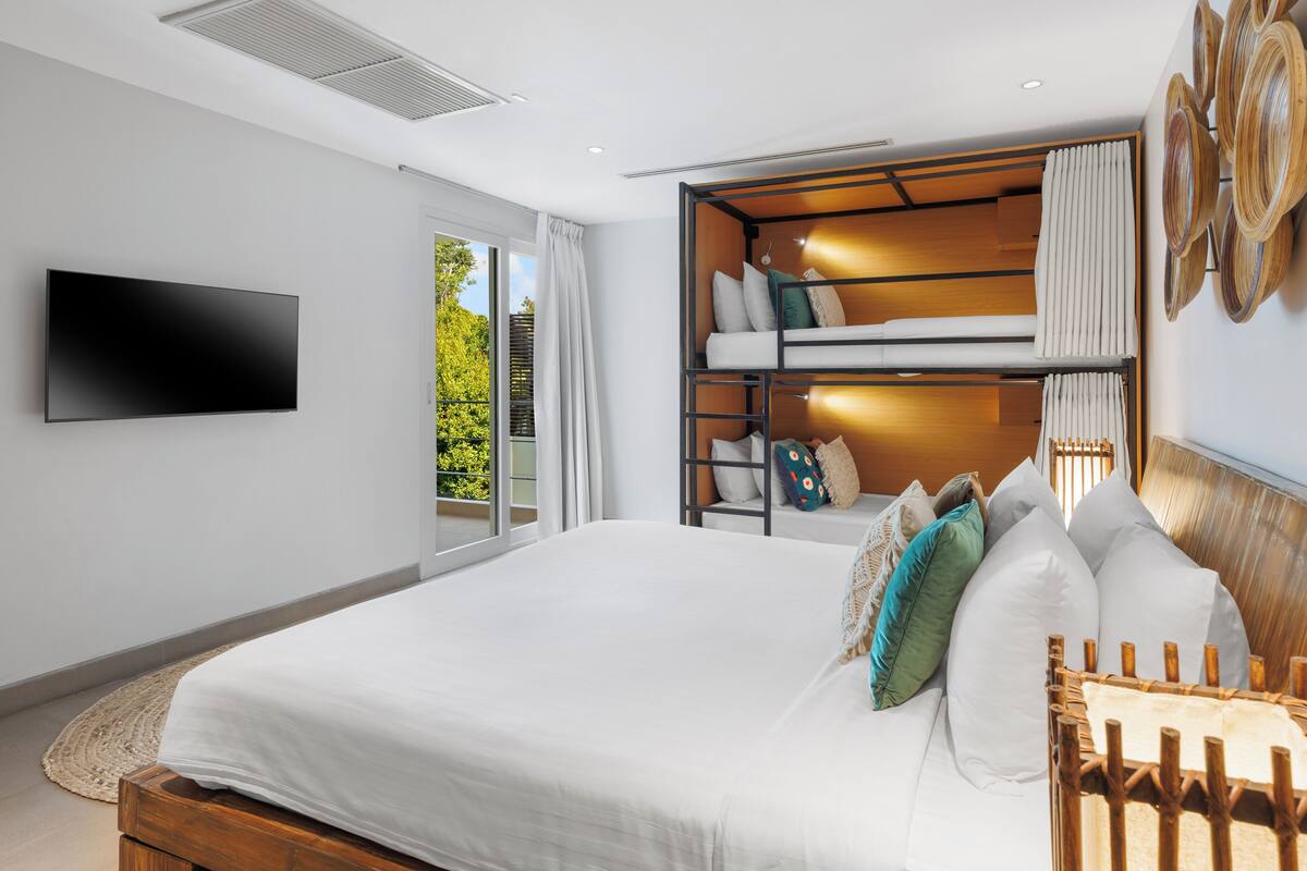 A modern bedroom with a large bed, a TV mounted on the wall, and a built-in seating area with cushions.