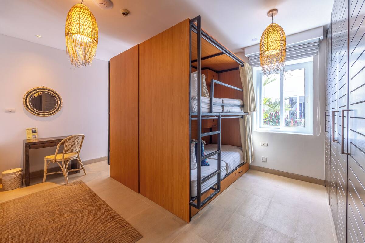 A compact bedroom with a built-in wardrobe, a desk, and a large window.