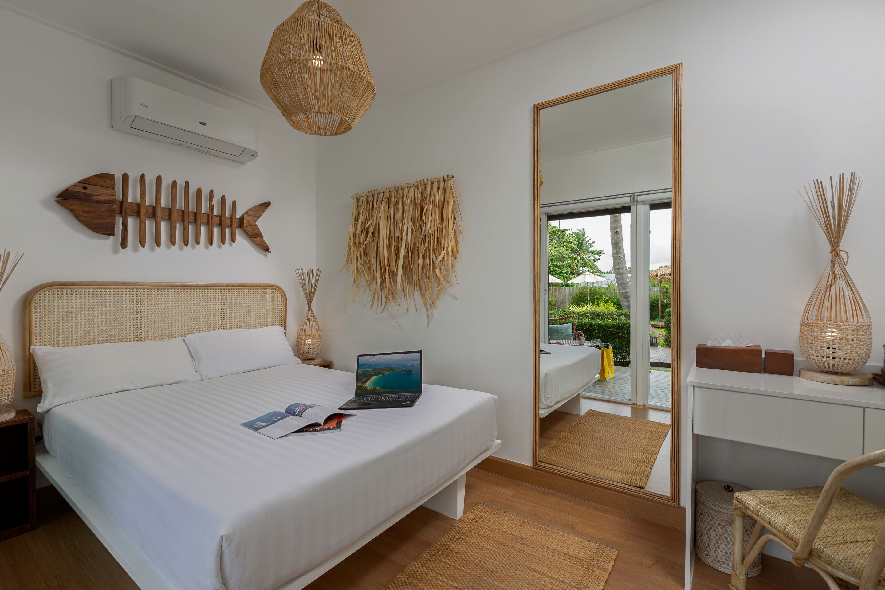 A bedroom with a bed, laptop, and a large mirror reflecting an outdoor view.
