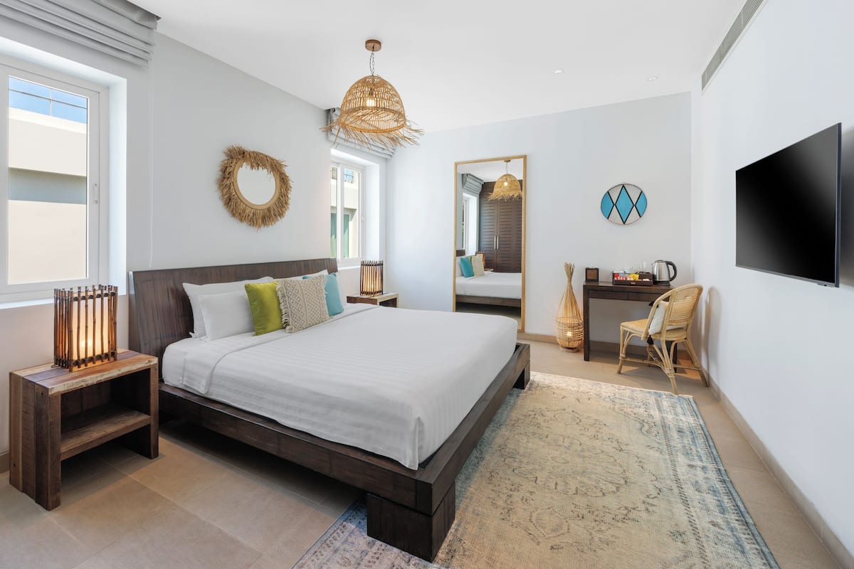A bedroom with a bed, bedside table, lamp, mirror, TV, and a desk with chair.