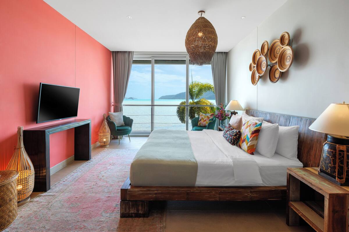 A hotel room with a large bed, a flat-screen TV, a view of the ocean, and a balcony.