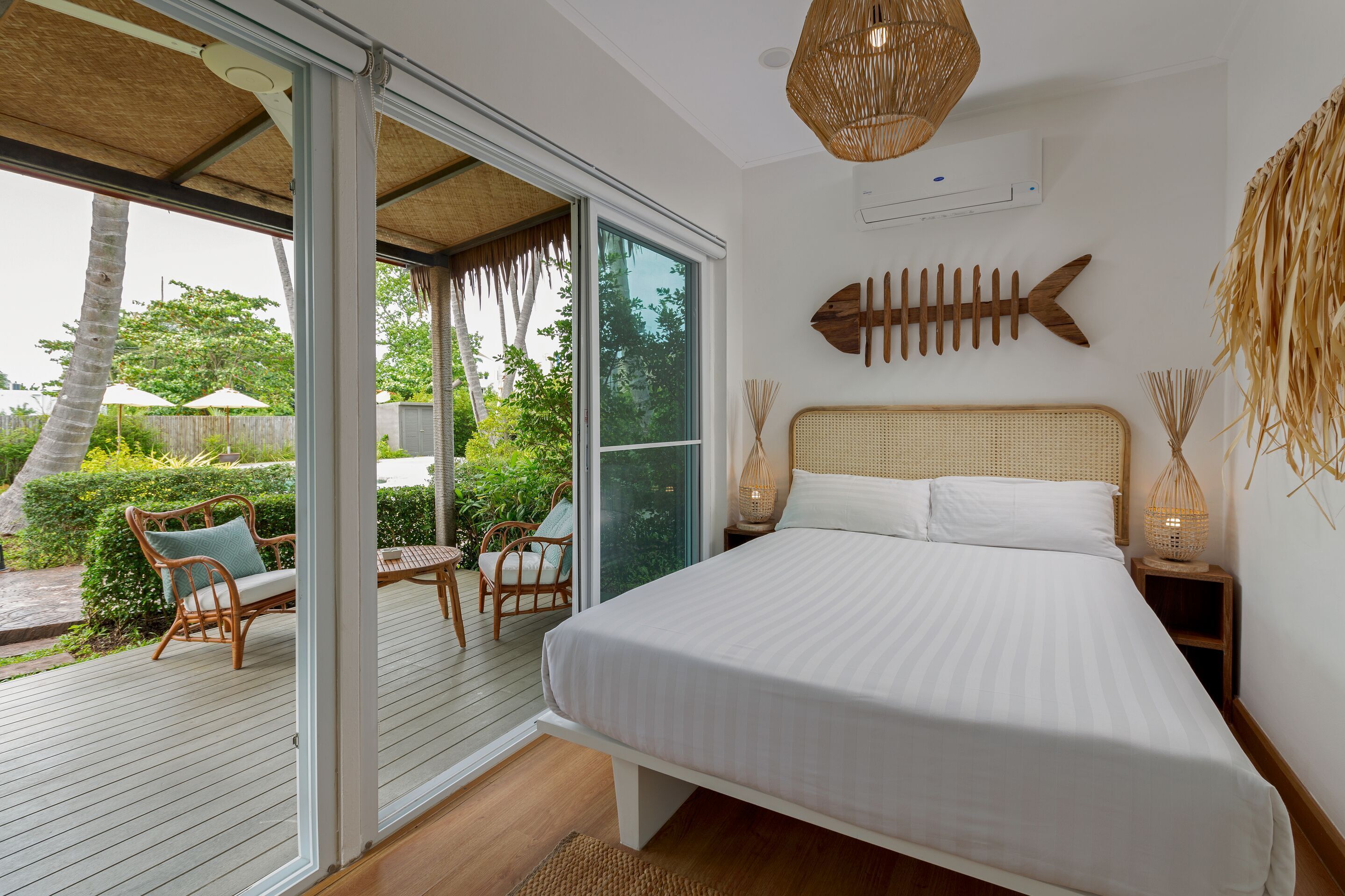 A bedroom with a large bed, a wicker headboard, a fish wall art, and a view of the outdoors.