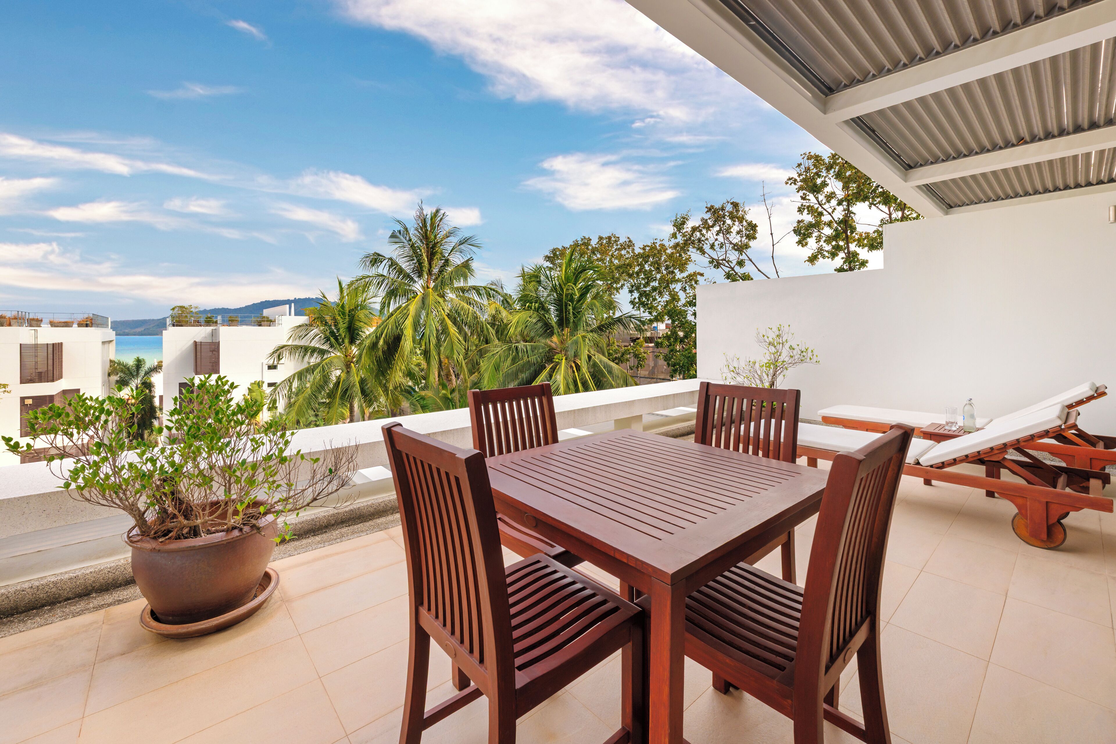 A terrace with a wooden table and chairs, a potted plant, and a reclining chair.