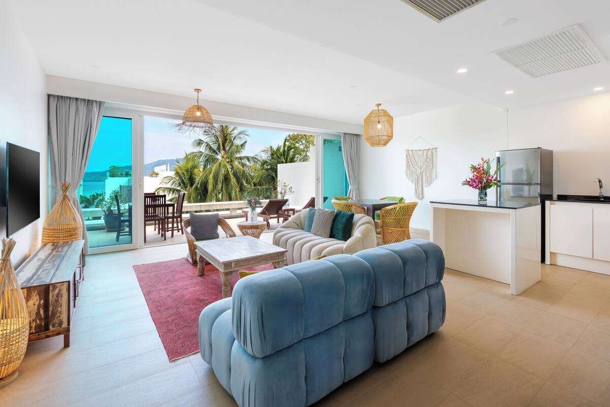 A modern living room with a sofa, dining area, kitchen, and a large sliding glass door leading to a balcony.