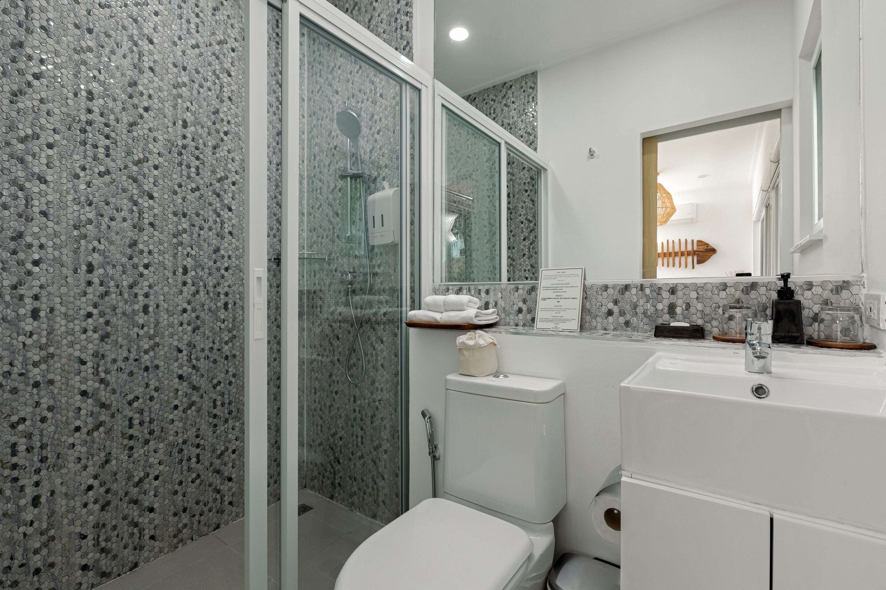 A bathroom with a glass shower enclosure, a white toilet, a sink with a mirror, and a towel rack.