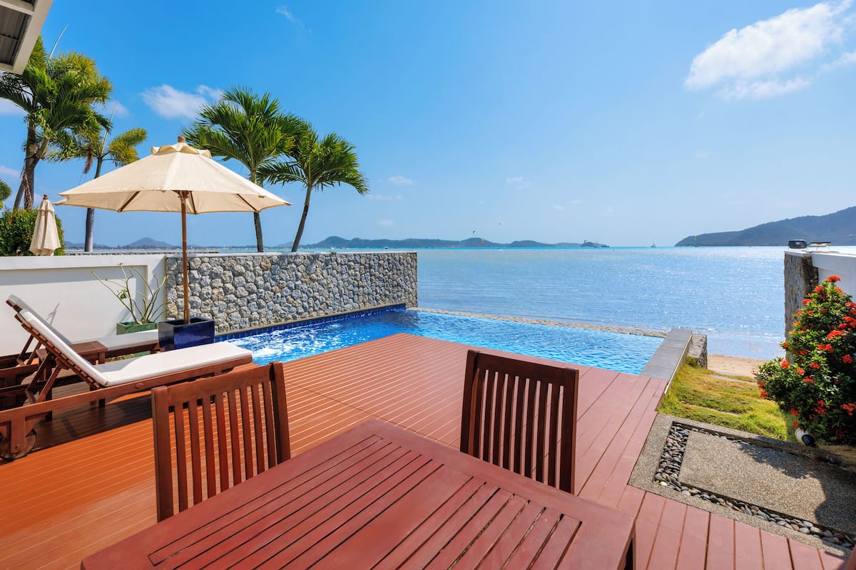 A wooden deck with a pool, lounge chairs, and a view of the sea.